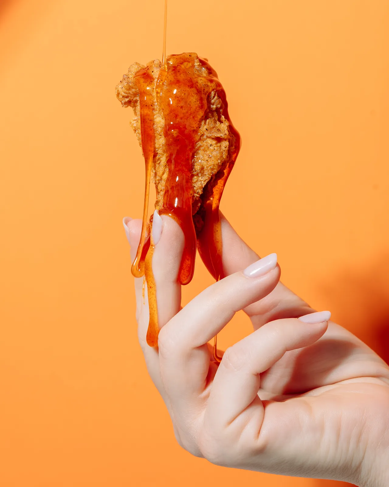 Strip Szechuan Hot Honey LBFC ținut în mână, pe fundal portocaliu